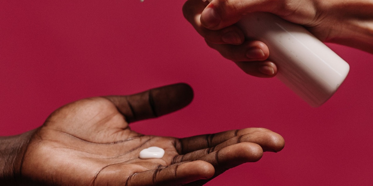 Moisturiser being dispensed onto the palm of a person with brown skin